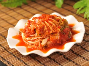 Bowel of bright red Kimchi as an example of Fermented foods. On a wicker placemat.