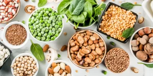 Over head shoot of nuts, seeds and green vegetables in individual bowels on a white table.