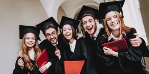 Group of 5 students with arms around each other and smiling in graduation outfits looking directly at the camera.